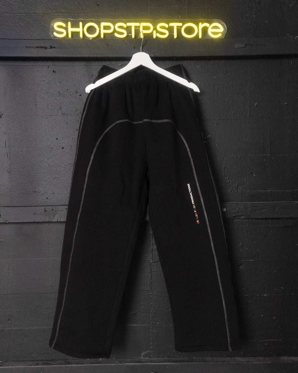 Black pants on a hanger in front of a Shopstpstore neon sign.