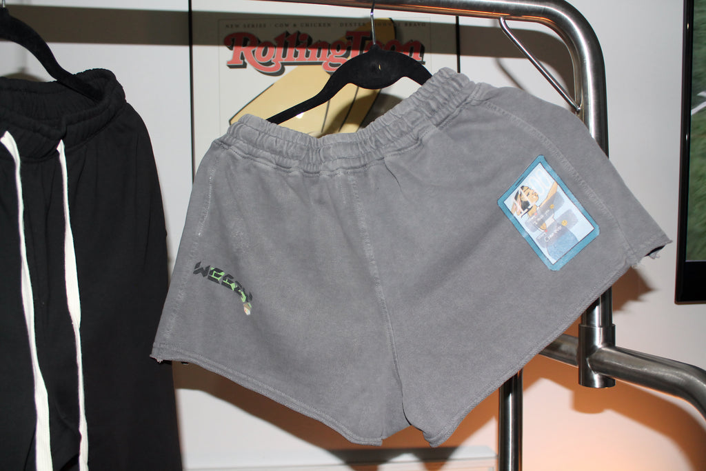 Gray shorts with a brand label on a rack in front of a Rolling Stones poster.