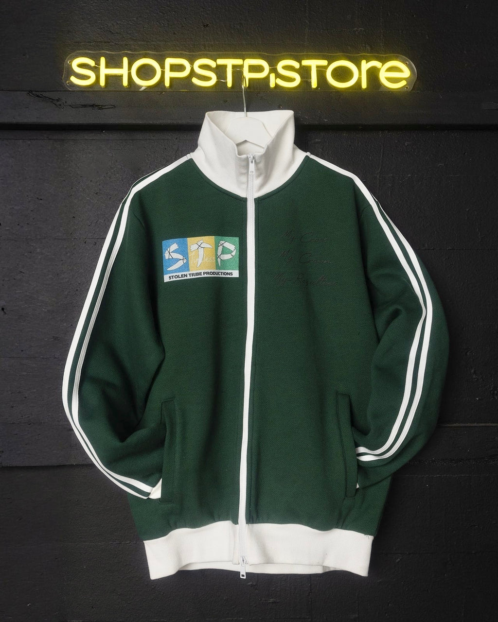 Green tracksuit with white accents on a dark background with 'SHOPSTP.STORE' neon sign.