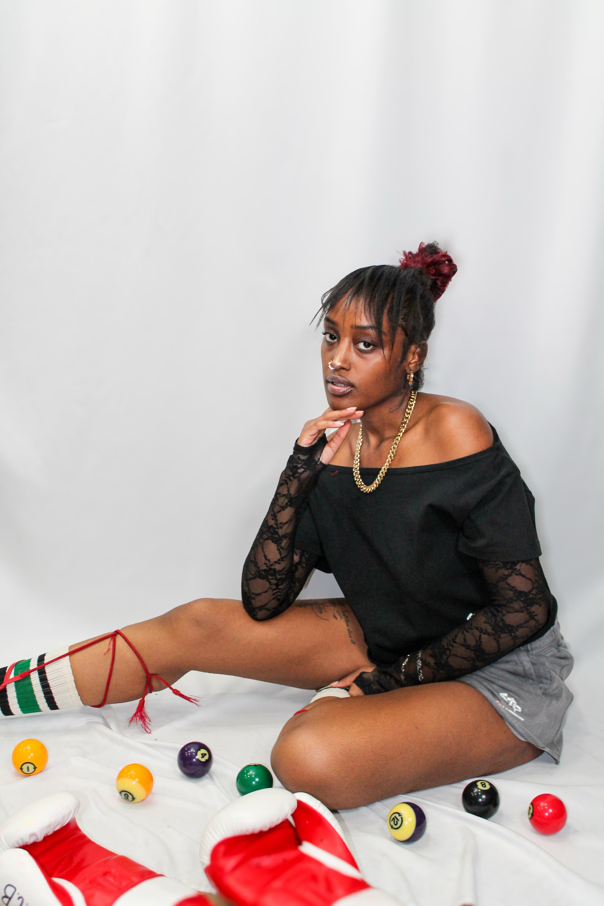 Woman sitting on a white surface with colorful balls around her, wearing a black top and gray shorts.