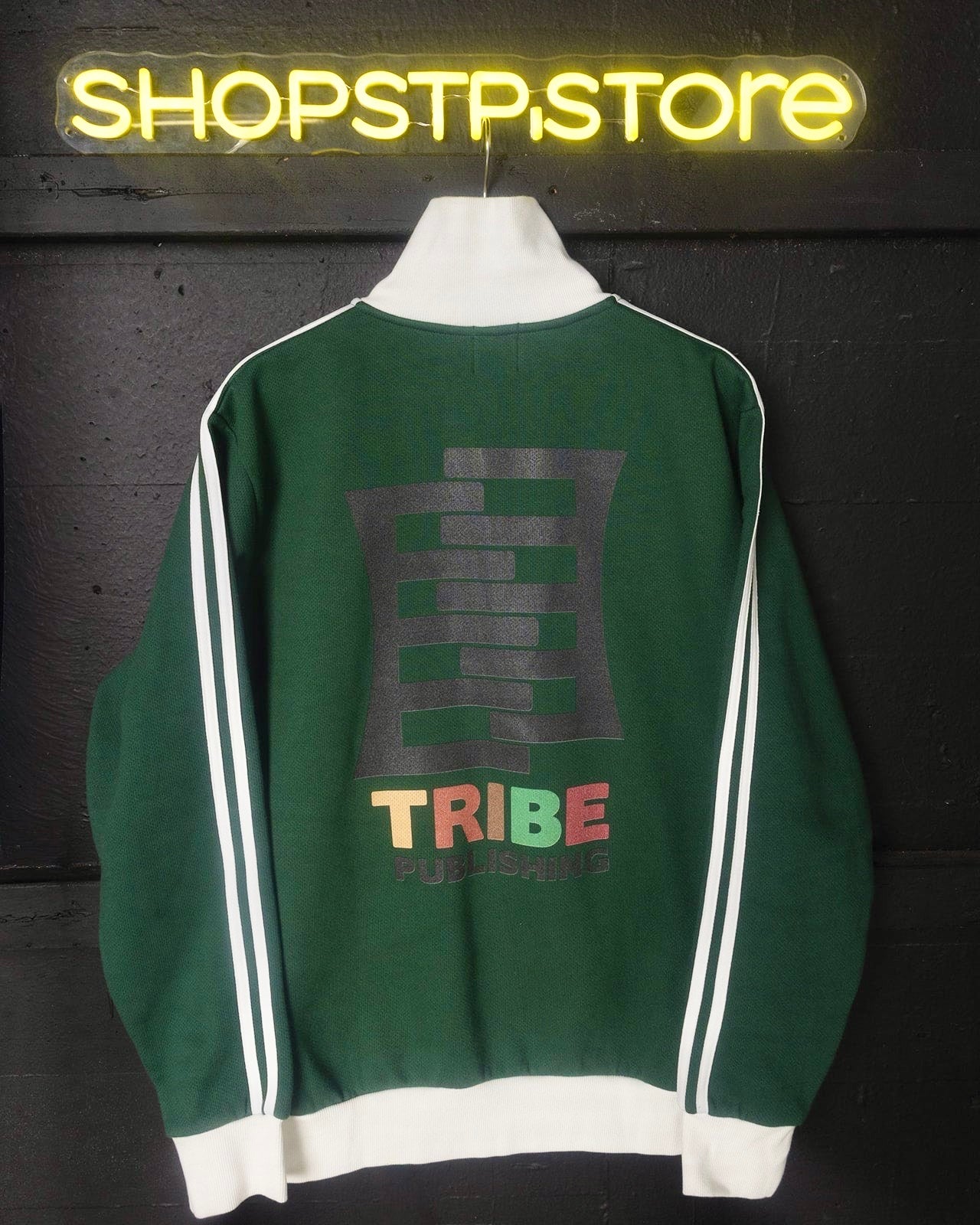 Green jacket with 'TRIBE' print on a dark background with neon sign