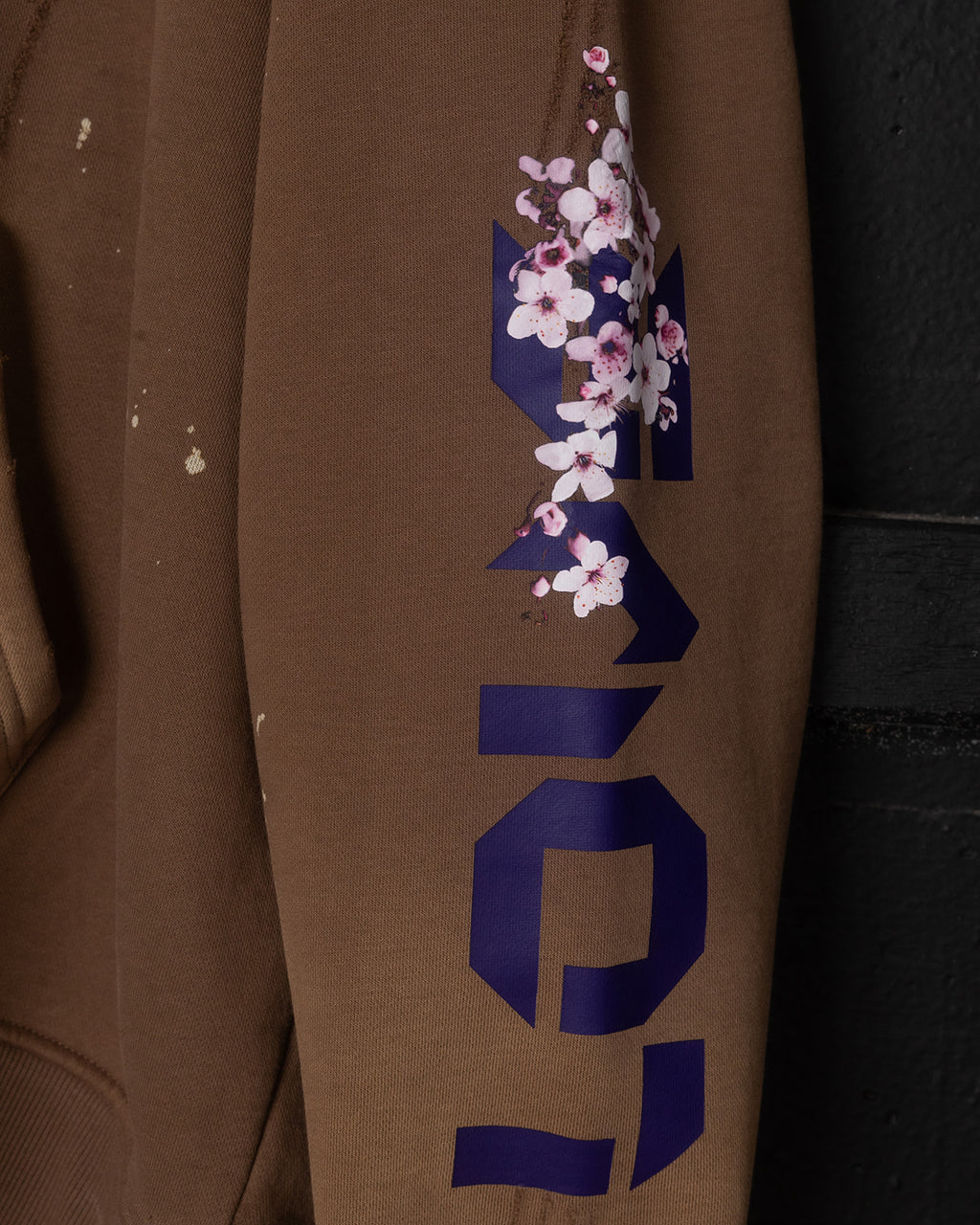 Brown sweatshirt with blue geometric design and floral elements on a dark background