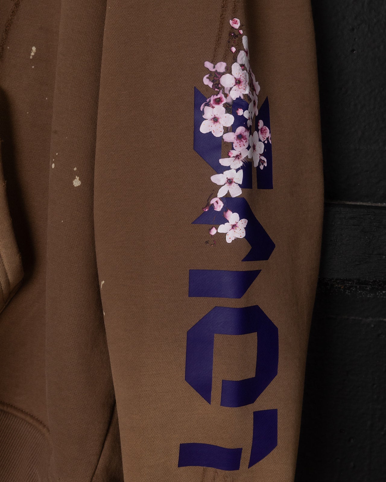 Brown sweatshirt with blue geometric design and floral elements on a dark background