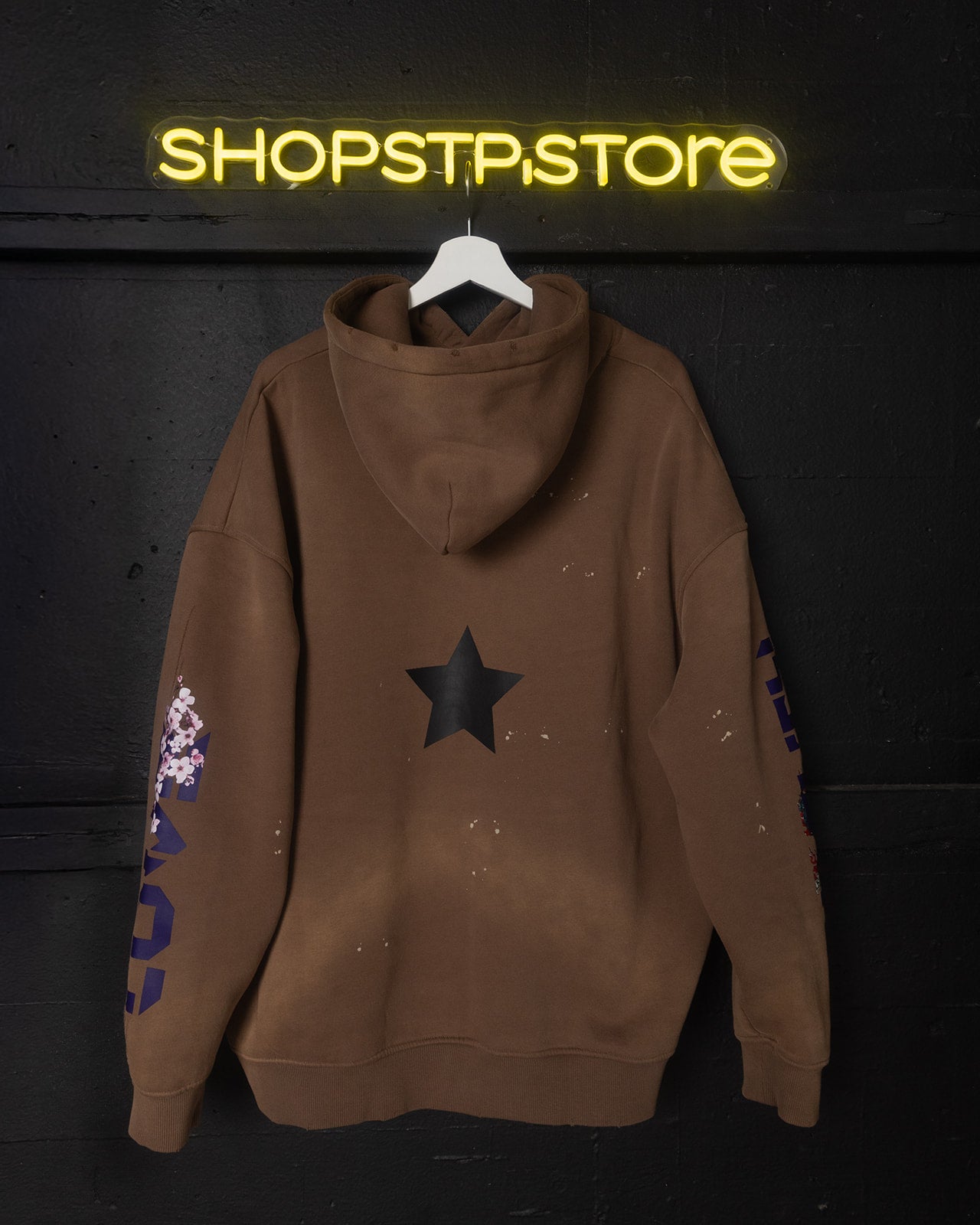 Brown hoodie with star design on a hanger against a dark background with 'SHOPSTP STORE' neon sign.