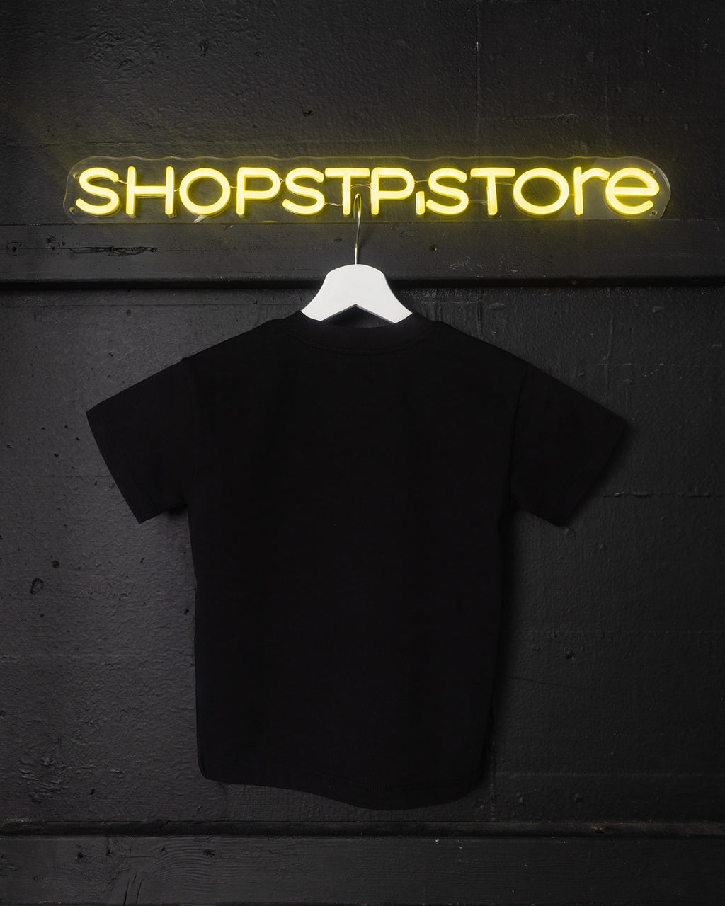 Black t-shirt on a hanger with 'SHOPSTP.STORE' neon sign in the background