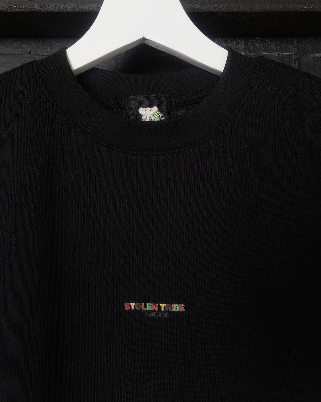 Black shirt with a colorful 'Stolen Tribe' logo on a white hanger against a dark background