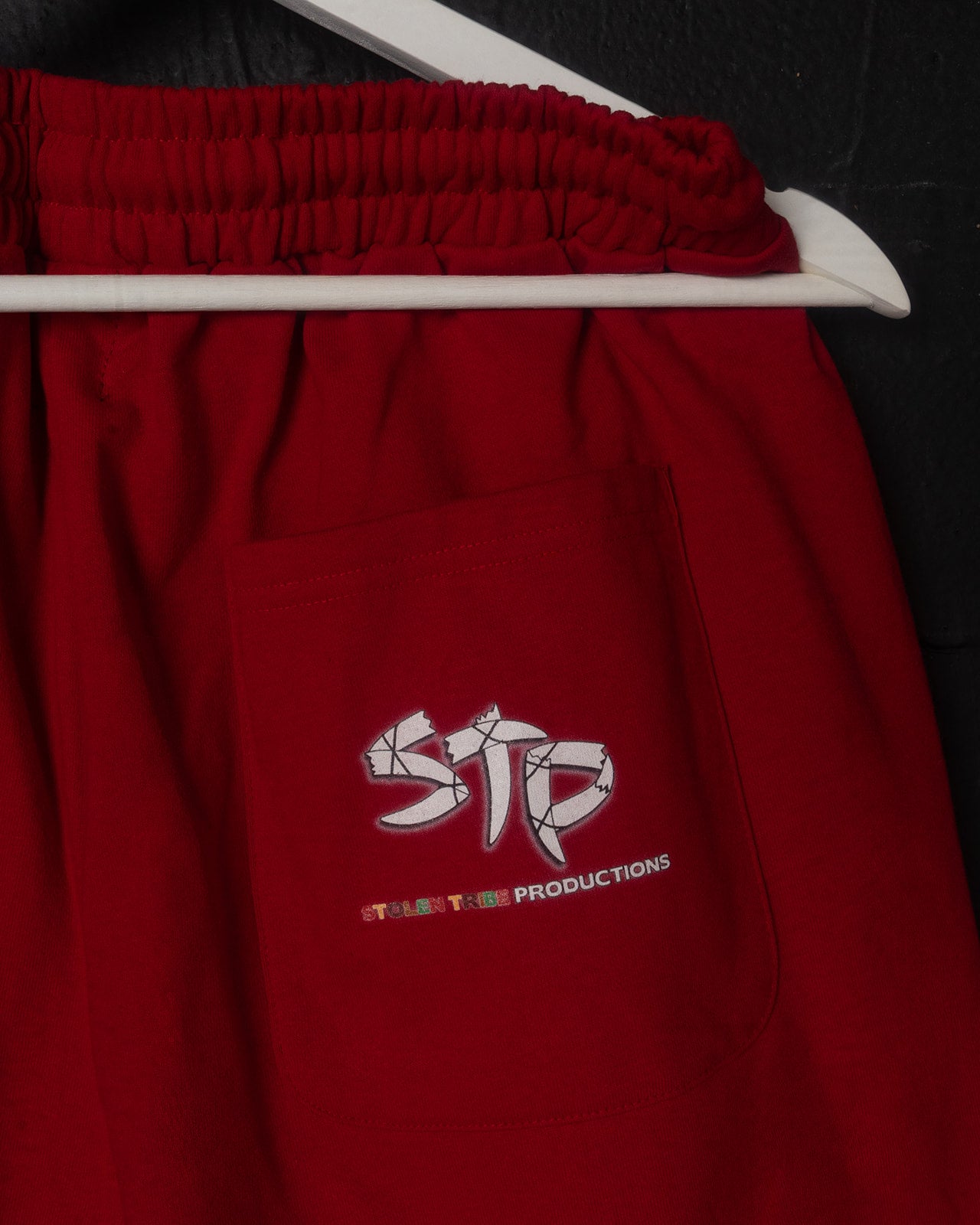 Red sweatpants with a logo on a hanger against a black background