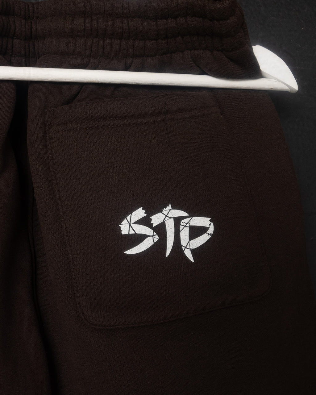 Brown pants with a white logo on the pocket against a dark background