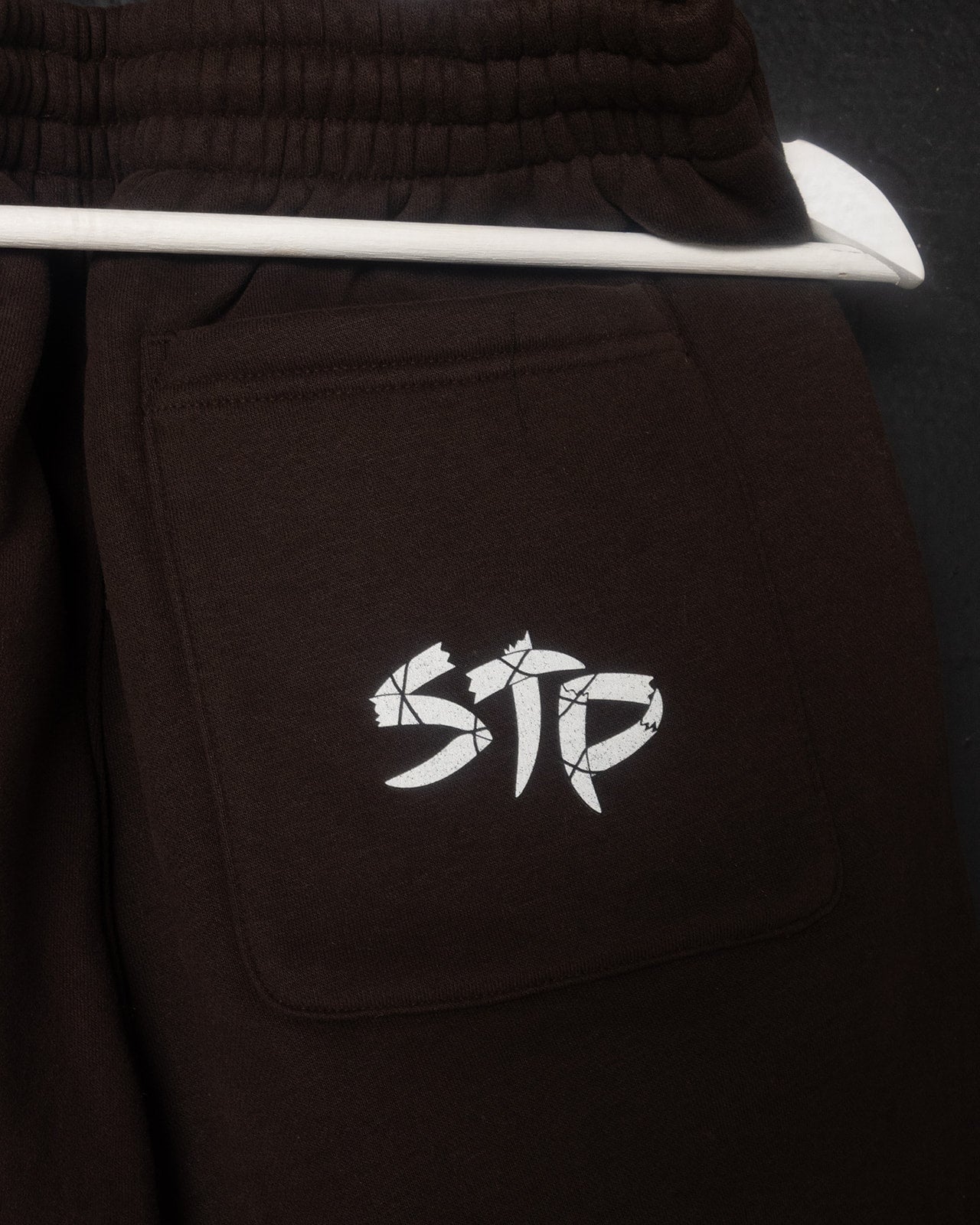 Brown pants with a white logo on the pocket against a dark background