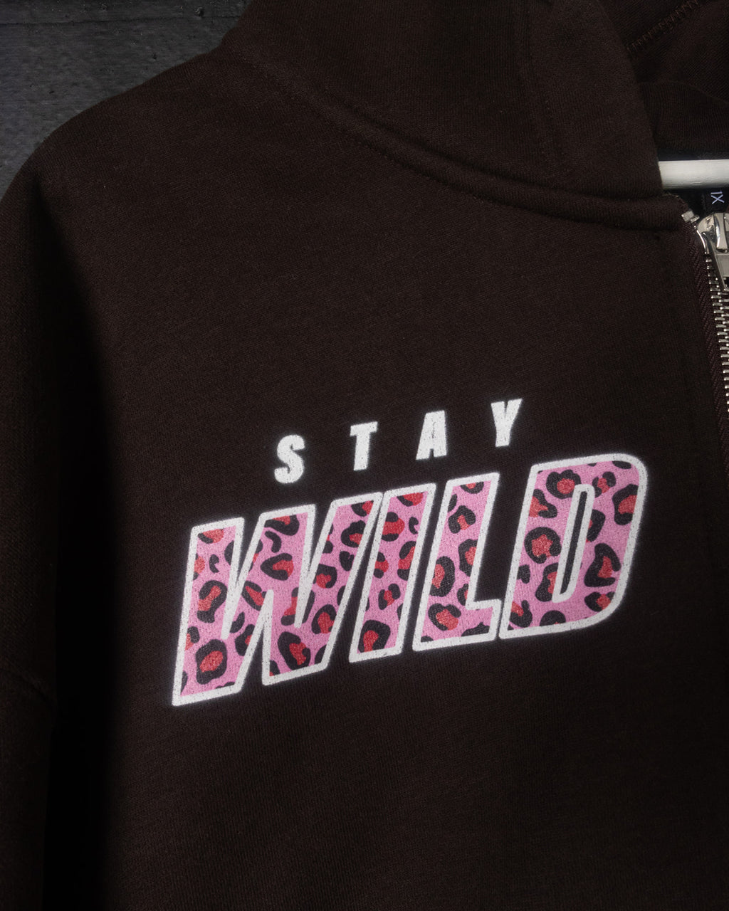 Black hoodie with 'Stay Wild' text in pink leopard print on a dark background