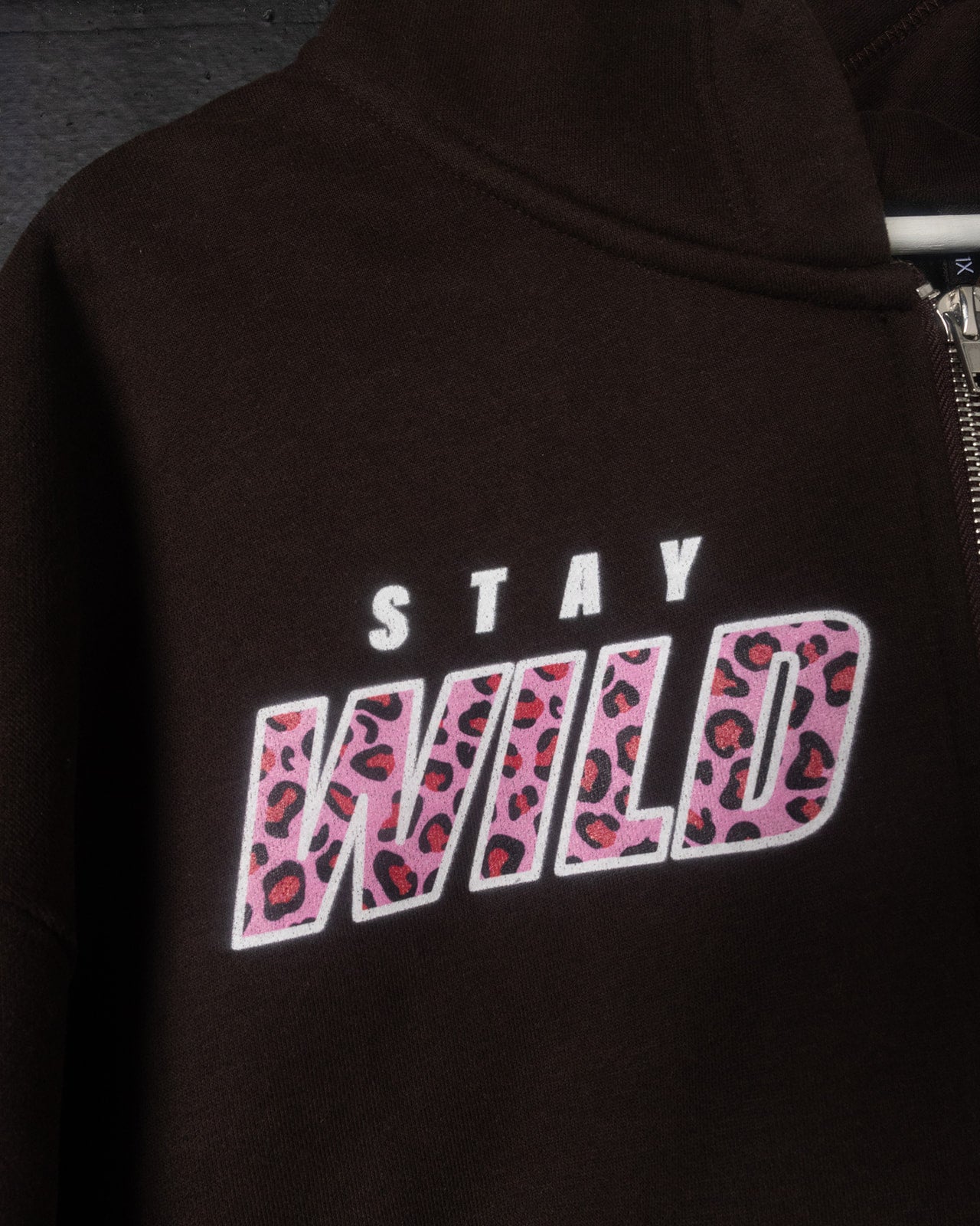 Black hoodie with 'Stay Wild' text in pink leopard print on a dark background