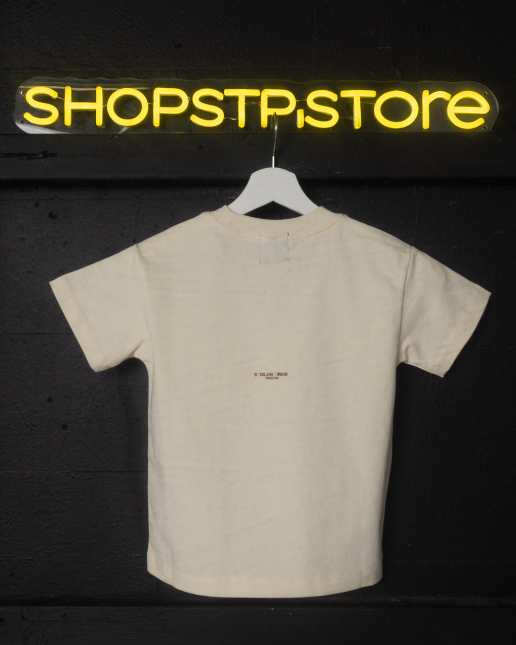 Beige t-shirt with a small logo on a hanger against a dark background with 'SHOPSTP.STORE' sign.