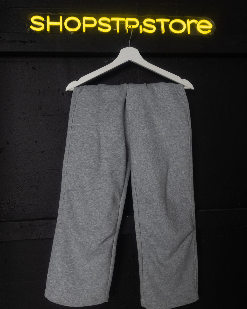 Gray pants on a hanger with 'Shopstpstore' neon sign in the background