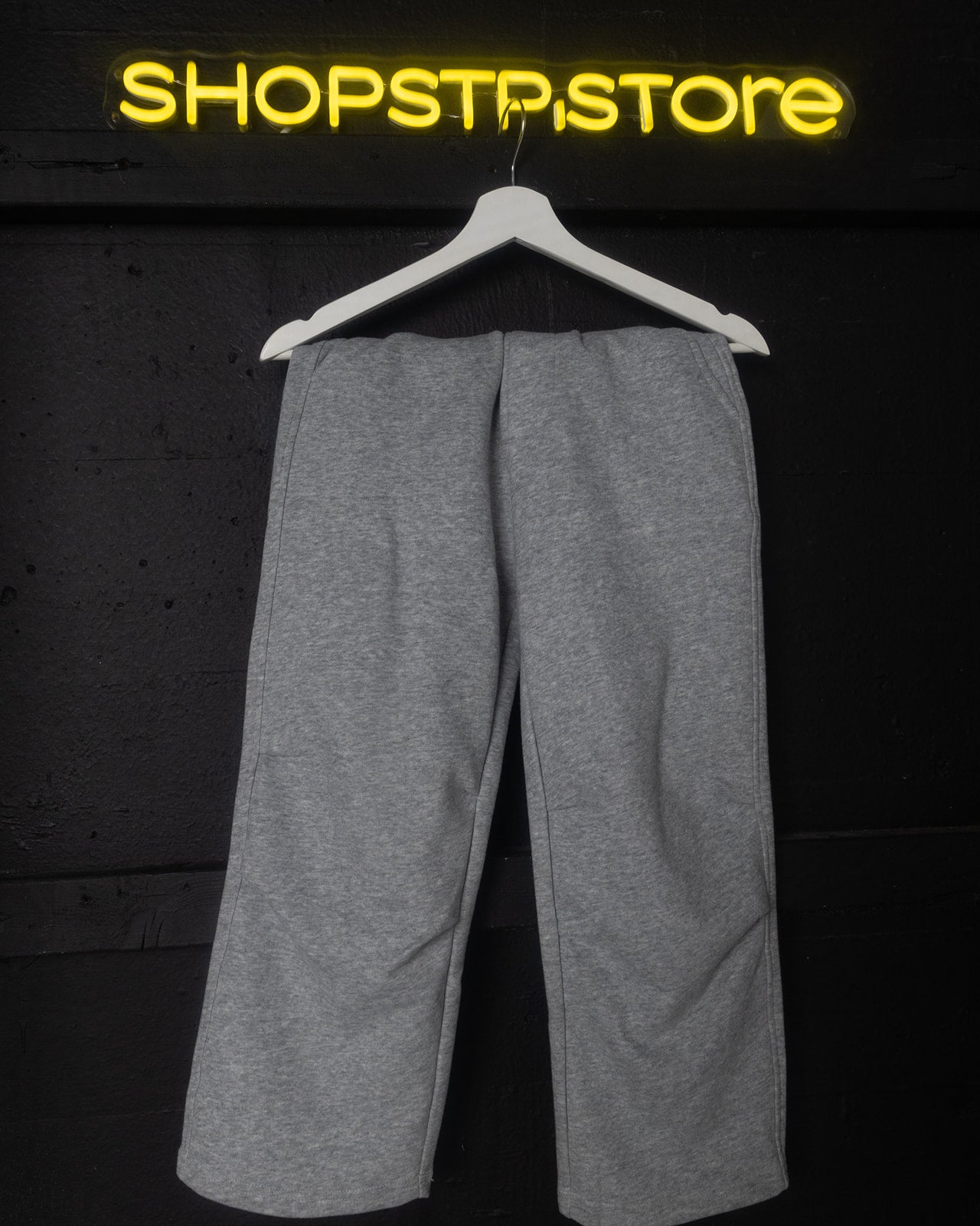 Gray pants on a hanger with 'Shopstpstore' neon sign in the background