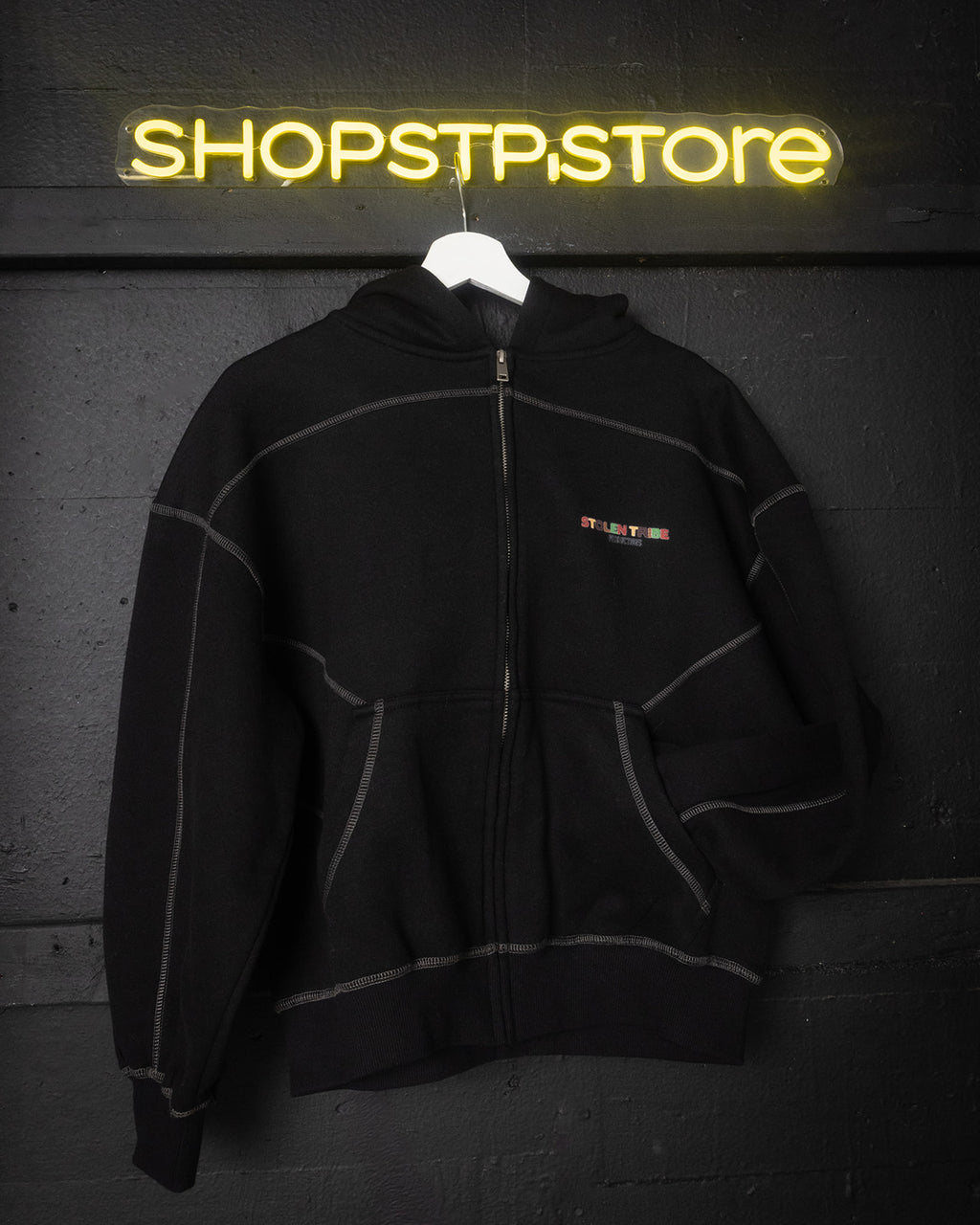 Black hoodie with a brand logo hanging in front of a neon 'SHOPSTP STORE' sign.
