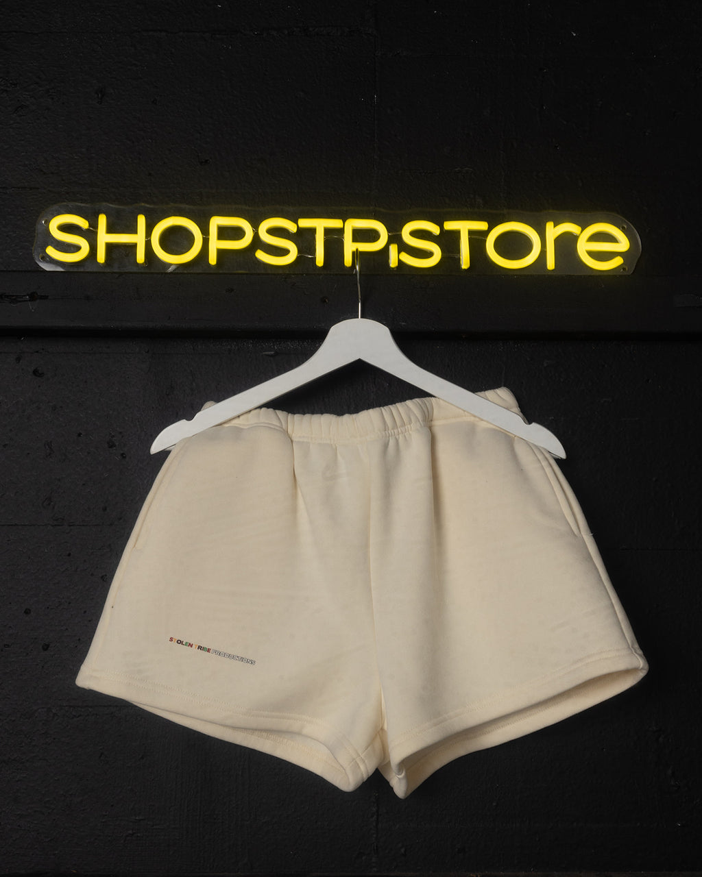 Beige shorts on a hanger with 'SHOPSTP.STORE' sign in yellow above on a black background