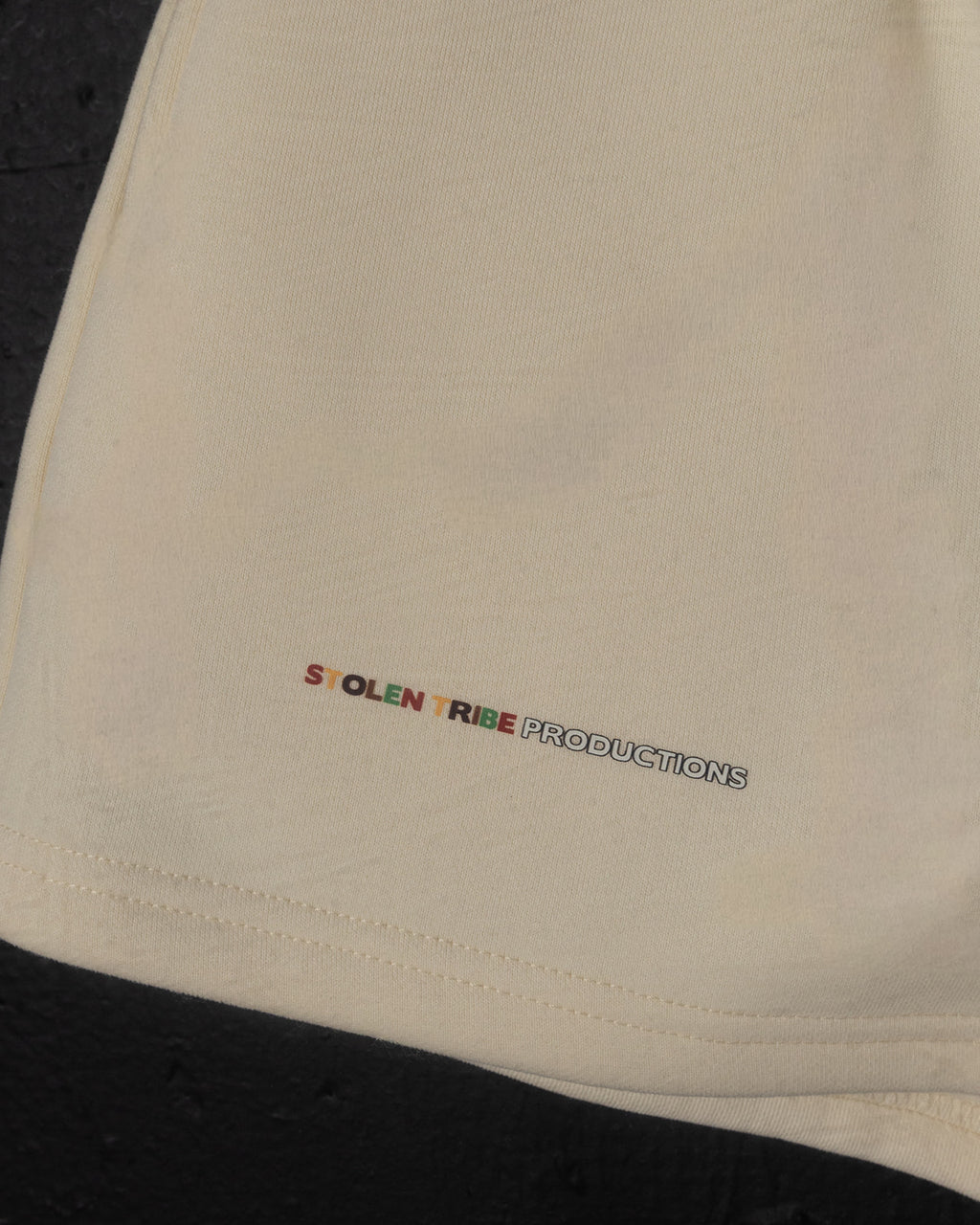 Beige fabric with 'STOLEN TRIBE PRODUCTIONS' logo embroidered on it.
