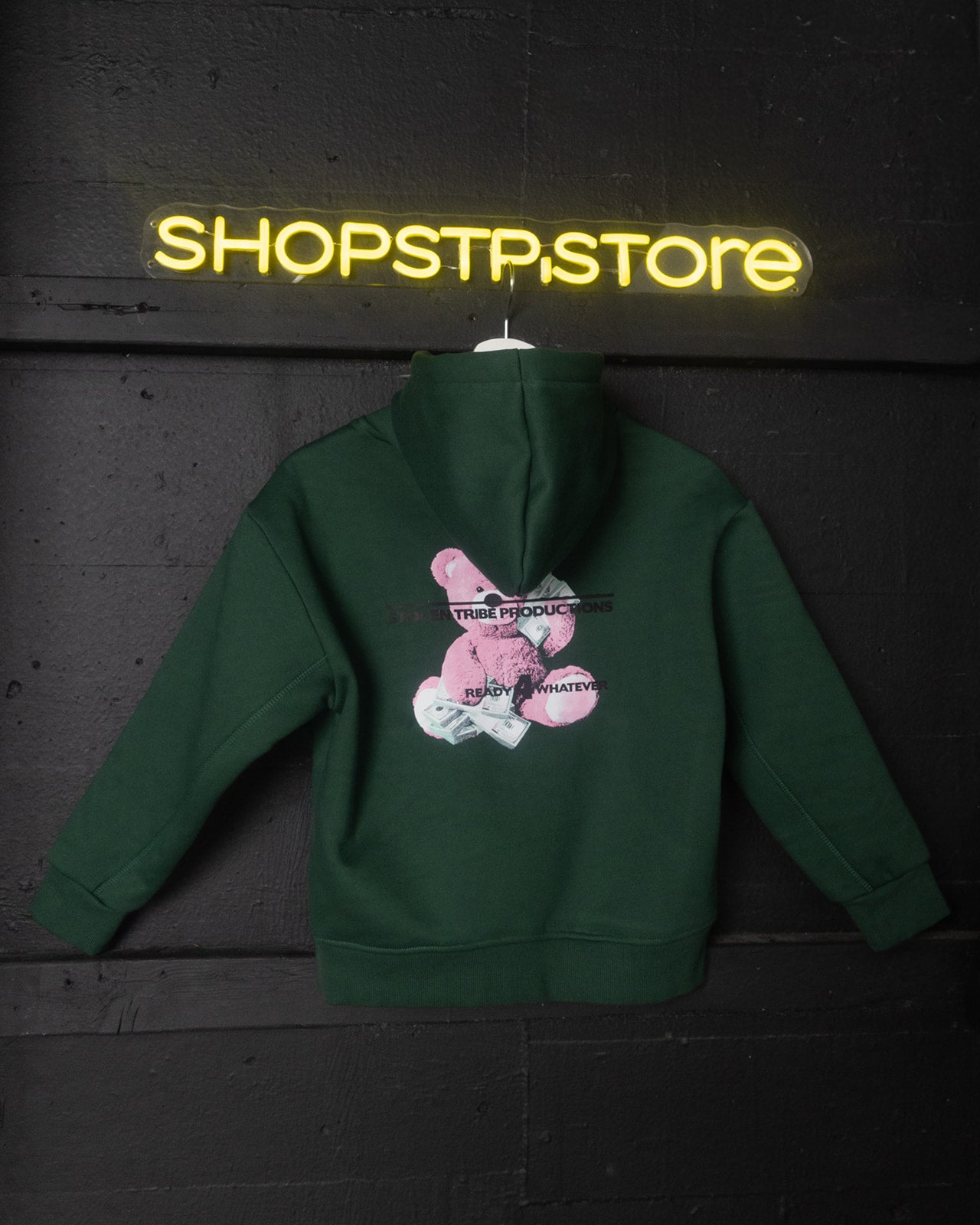Green hoodie with a graphic design on the back, displayed against a dark background with 'SHOPSTP.STORE' neon sign.