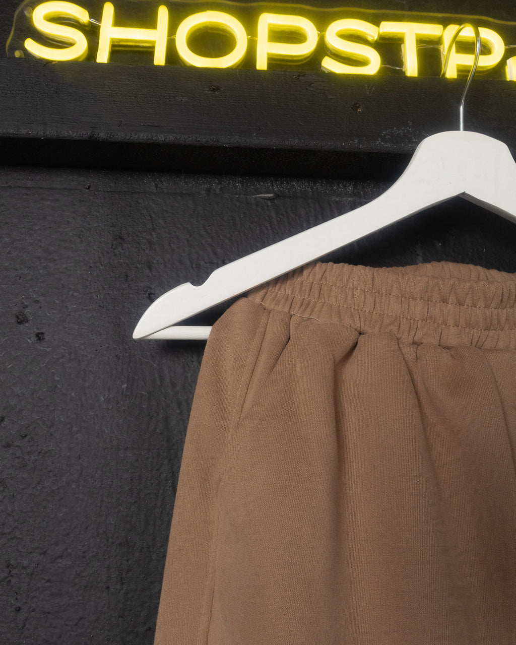 Brown pants on a white hanger against a dark background with 'SHOPSTP neon sign.