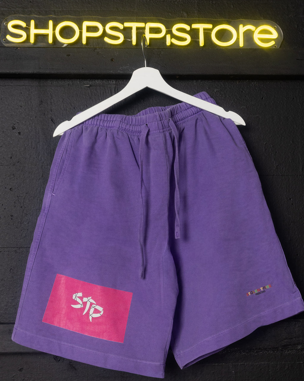 Purple shorts with a logo on a hanger against a dark background with 'SHOPSTP STORE' sign.