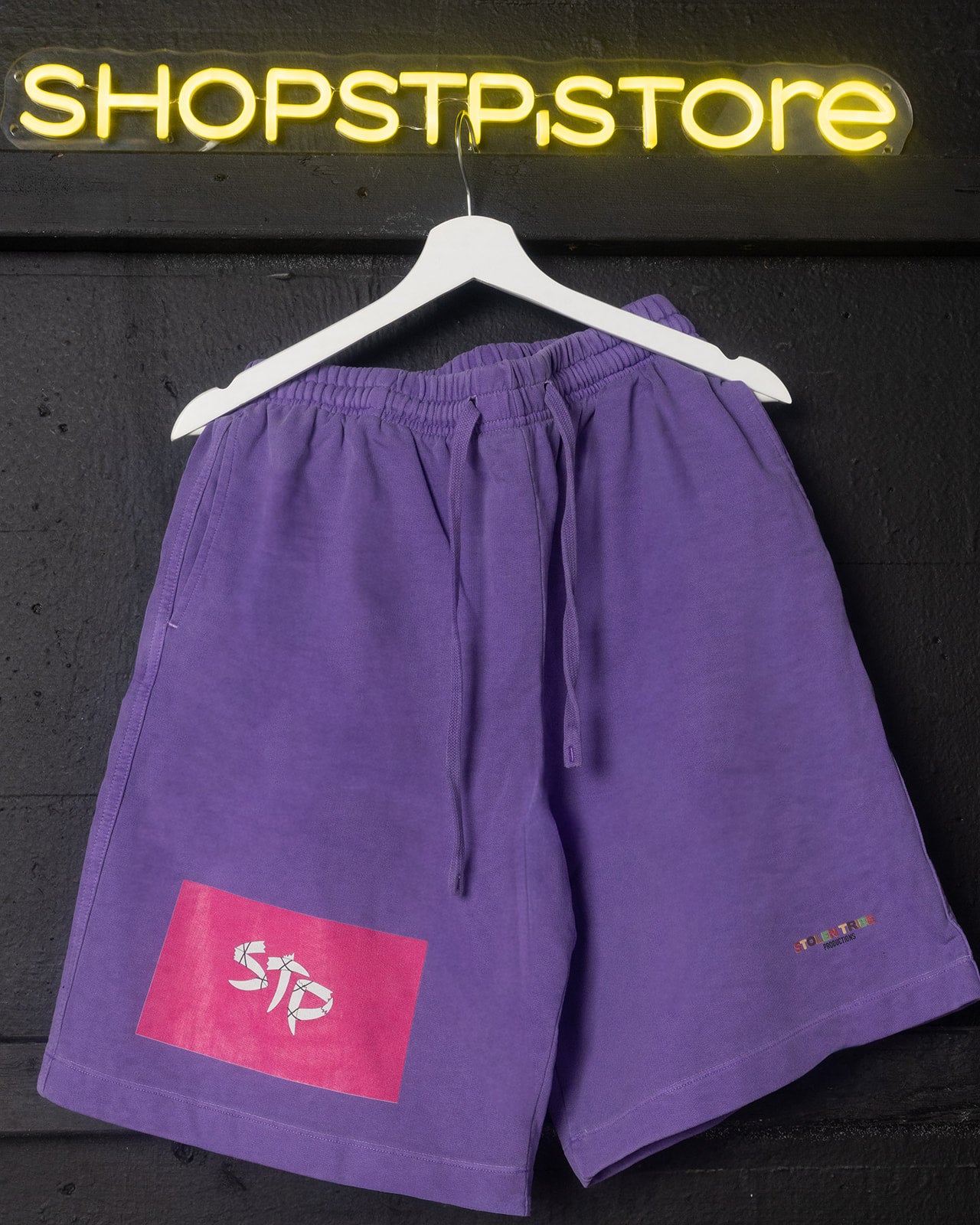 Purple shorts with a logo on a hanger against a dark background with 'SHOPSTP STORE' sign.