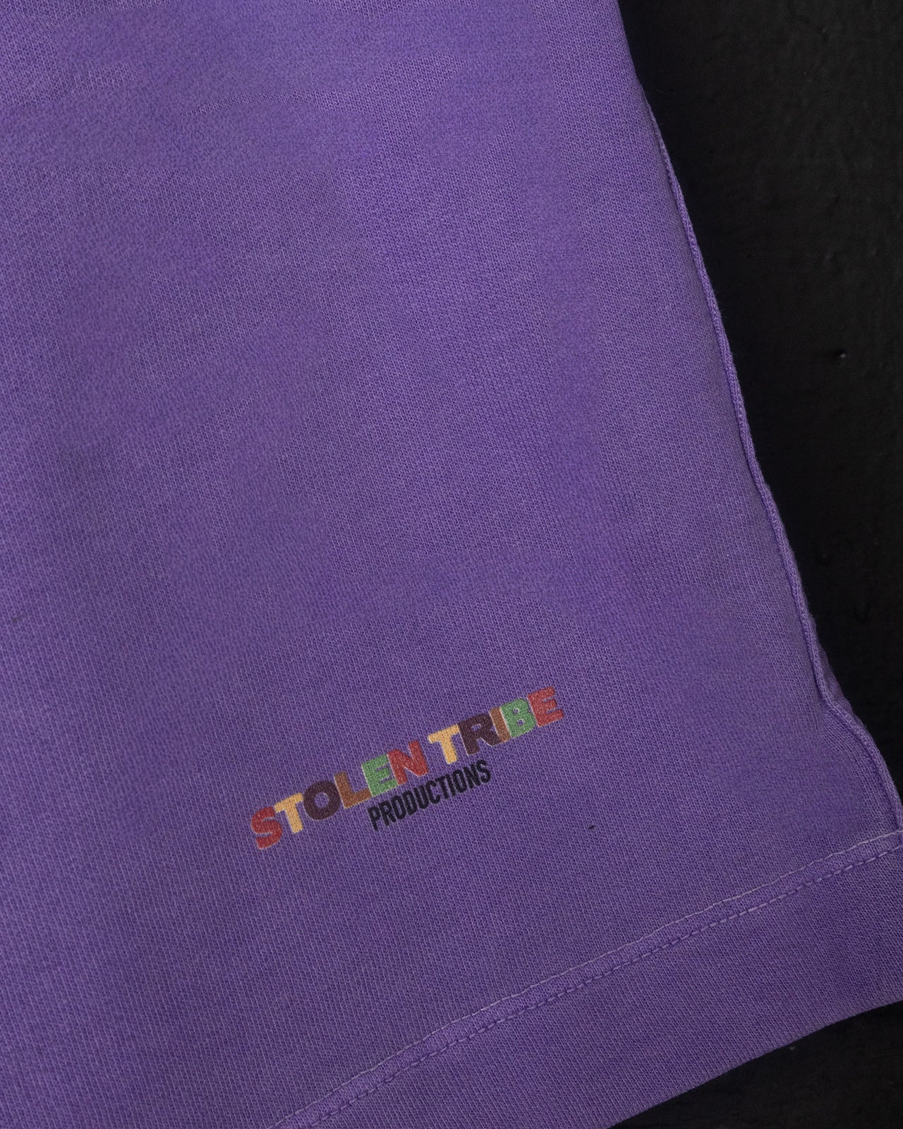 Close-up of a purple garment with 'STOLEN TRIBE PRODUCTIONS' embroidered on it.
