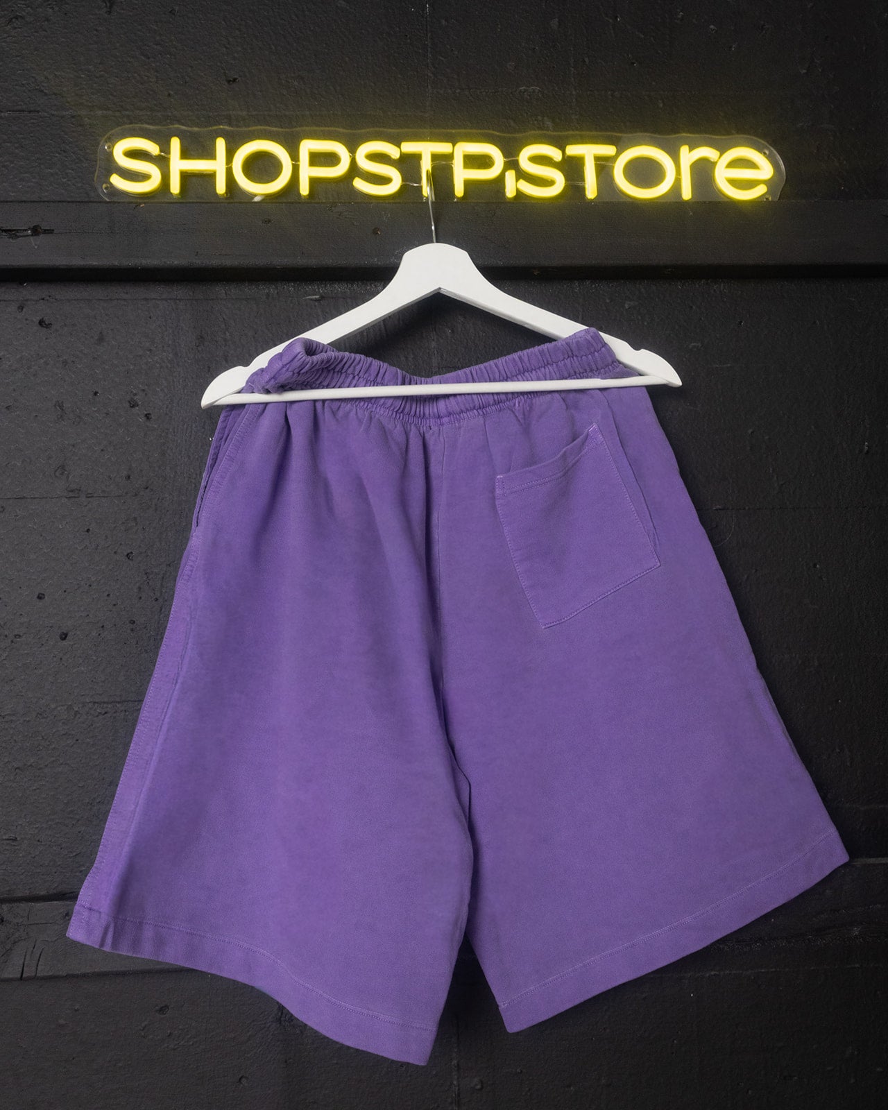 Purple shorts on a hanger with 'SHOPSTP.STORE' neon sign in the background