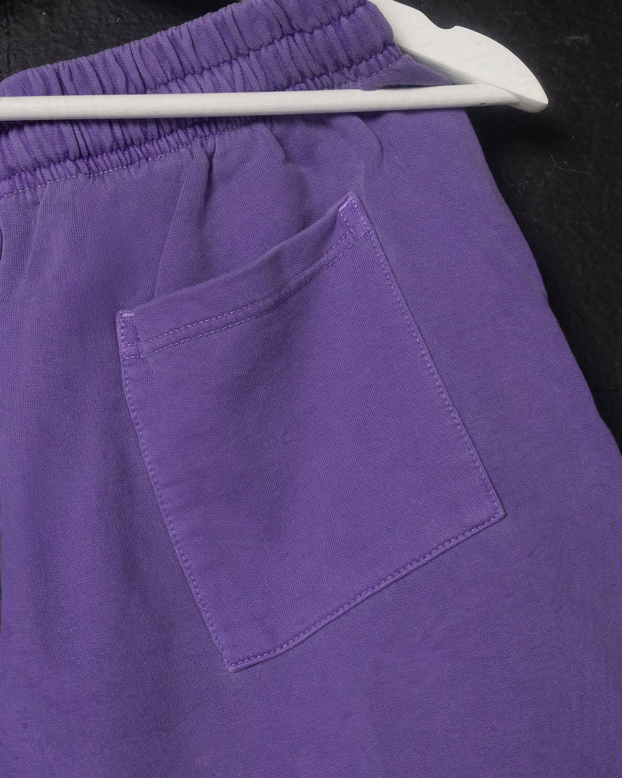 Purple shorts with a pocket on a hanger against a black background