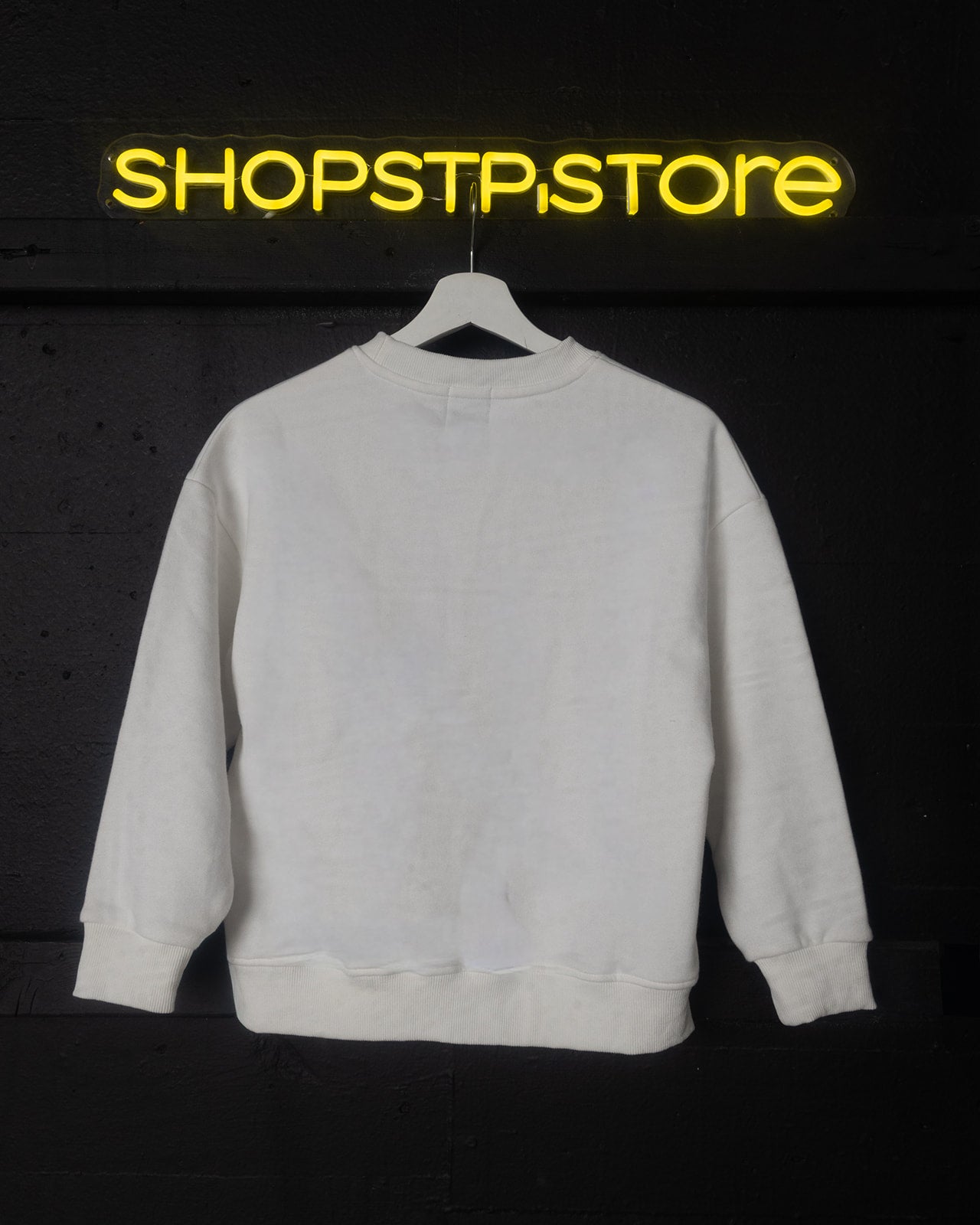 White sweatshirt on a hanger with 'SHOPSTP STORE' neon sign in the background