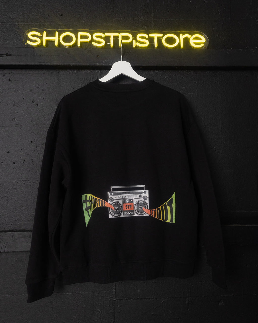 Black sweatshirt with a graphic design hanging in front of a neon 'SHOPSTPSTORE' sign.