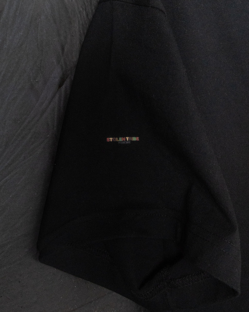 Black shirt with a small orange logo on the chest against a gray background