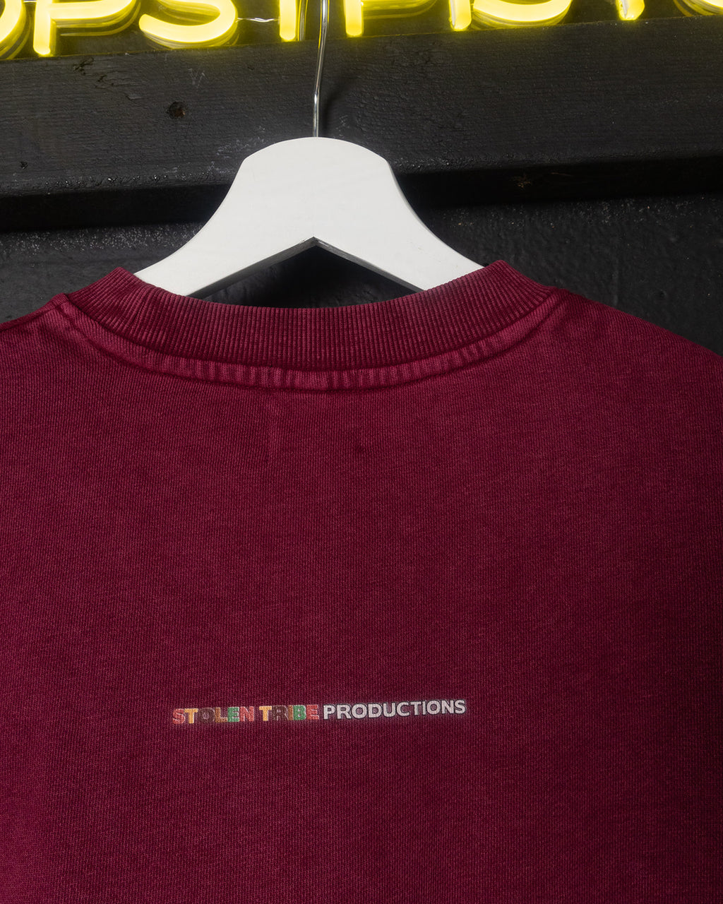 Maroon sweatshirt with 'Stolen Tribe Productions' logo on a hanger against a dark background.