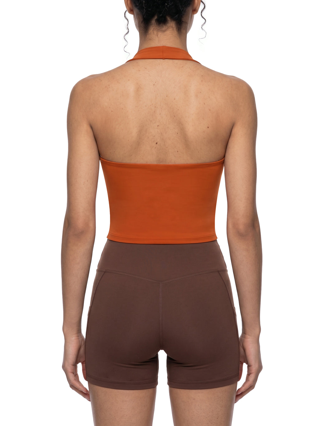 Person wearing an orange halter top and brown shorts on a white background