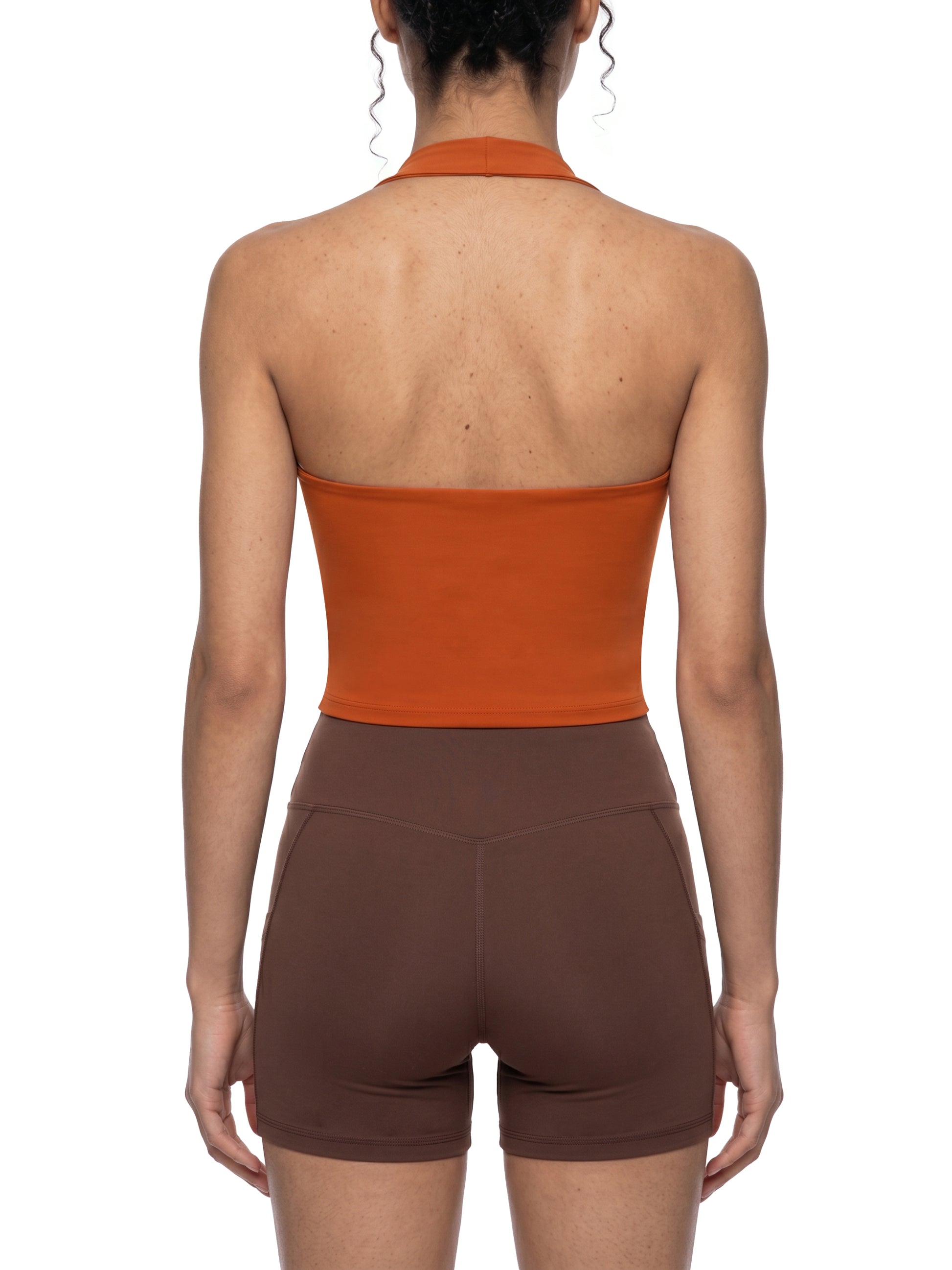 Person wearing an orange halter top and brown shorts on a white background