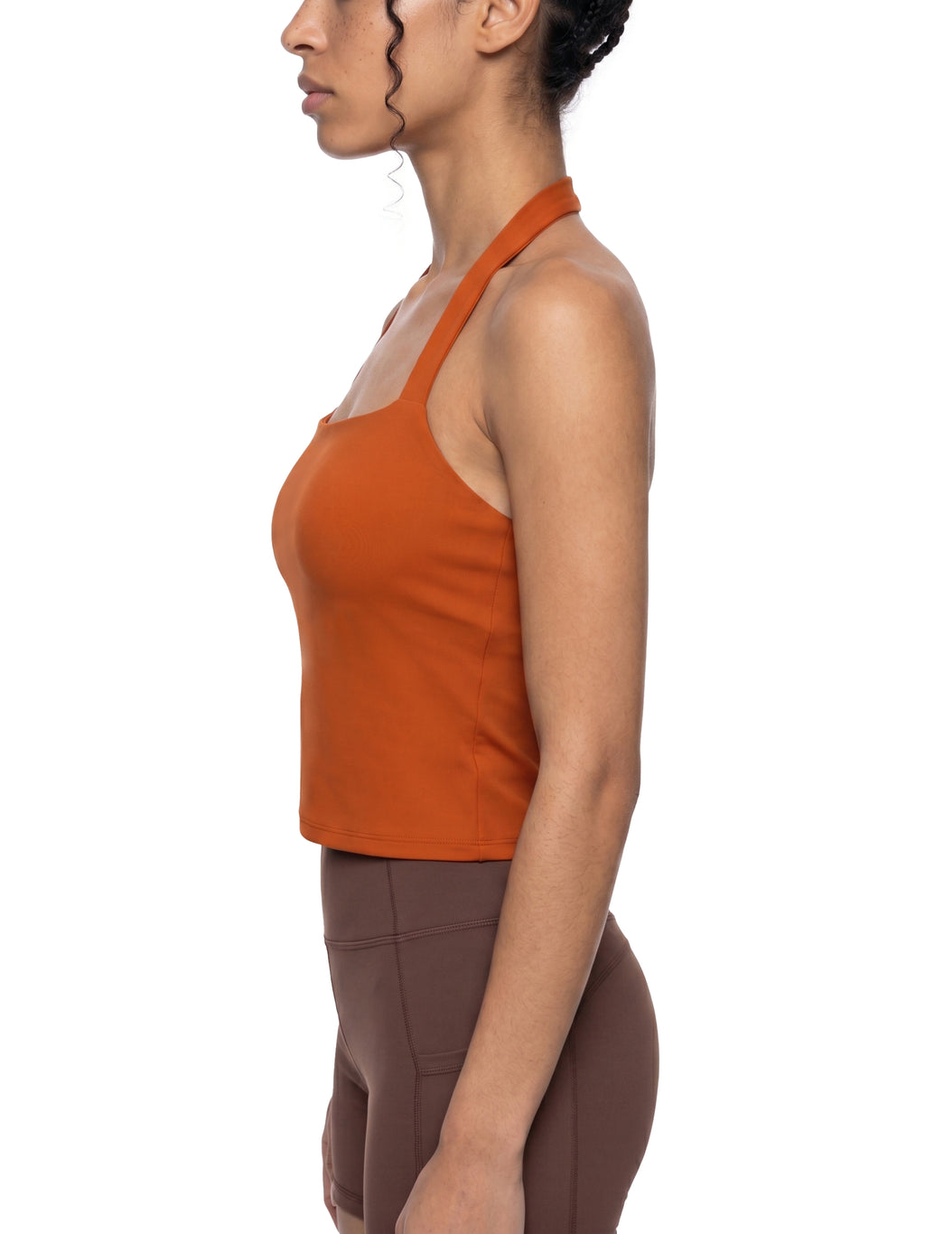 Woman wearing an orange tank top and brown leggings on a white background