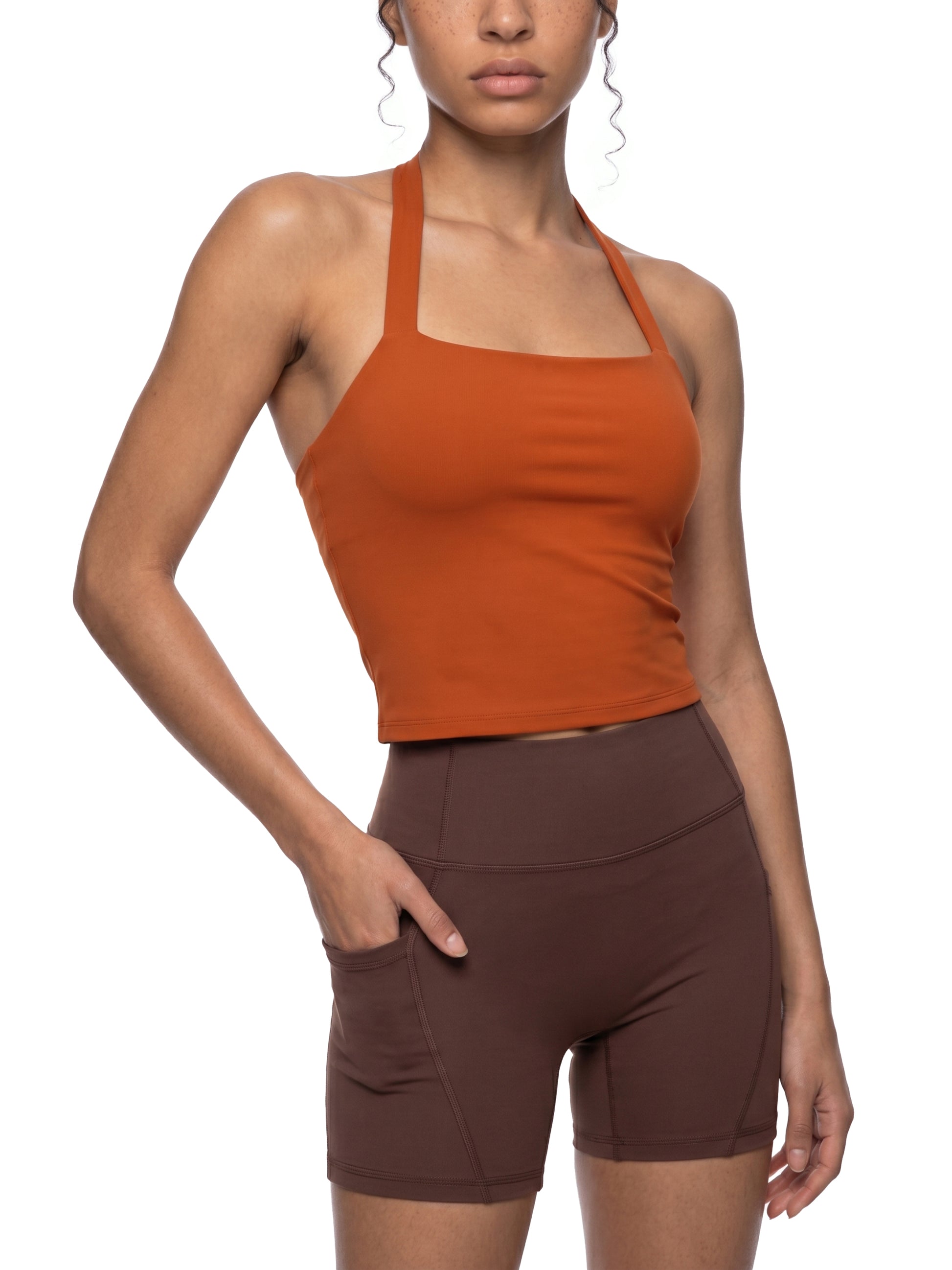 Woman wearing an orange tank top and brown shorts on a white background