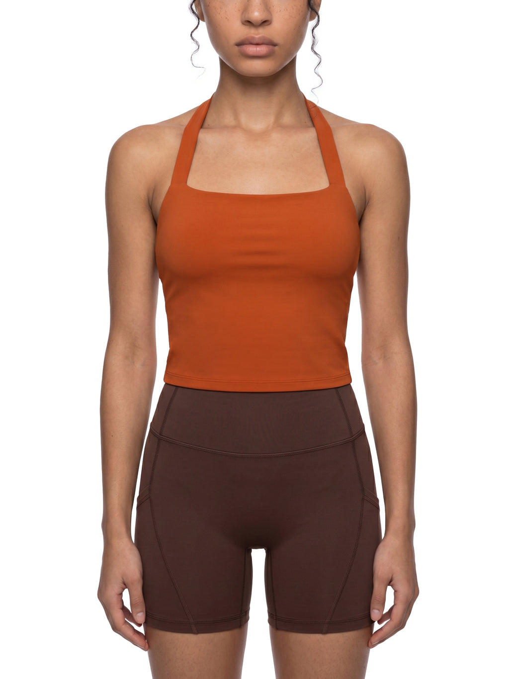 Person wearing an orange tank top and brown shorts on a white background
