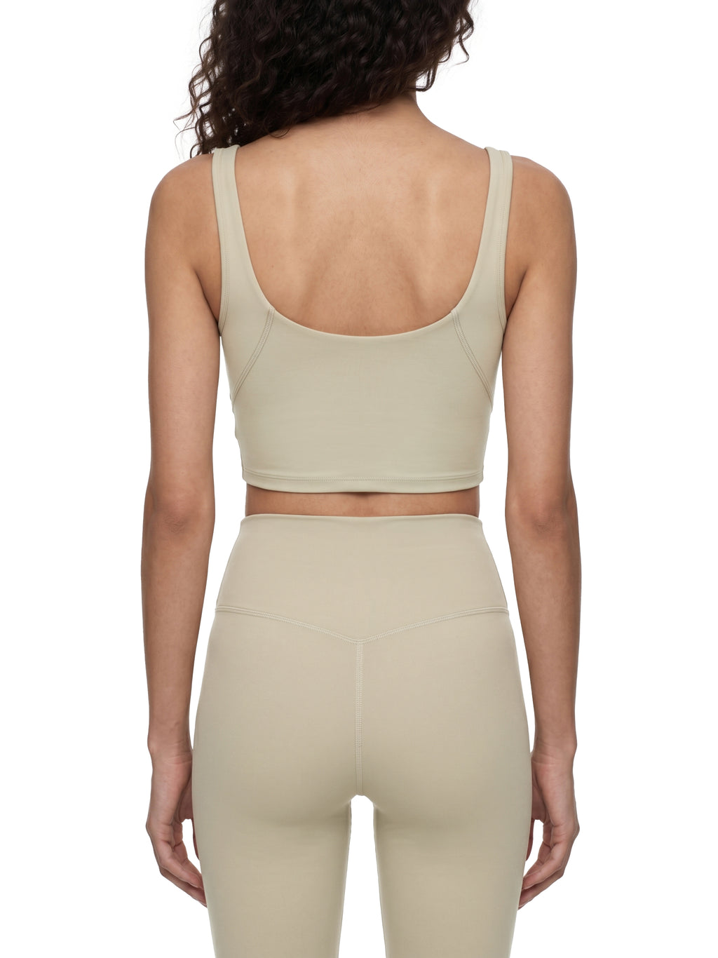 Person wearing a beige sports bra and leggings set on a white background