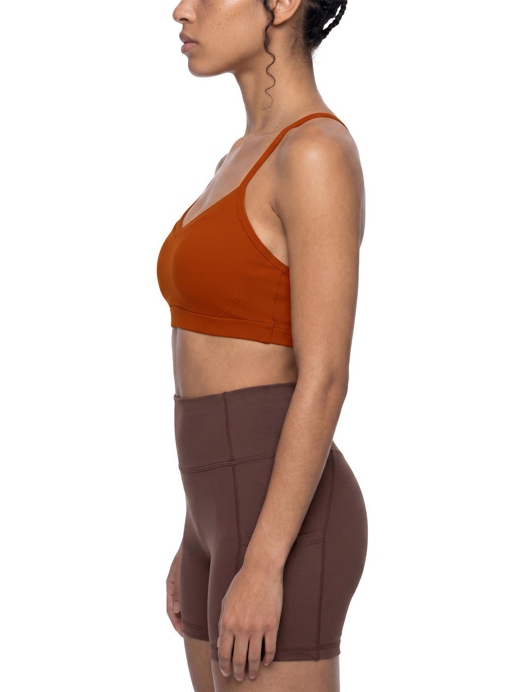 Woman wearing a rust-colored sports bra and brown shorts on a white background