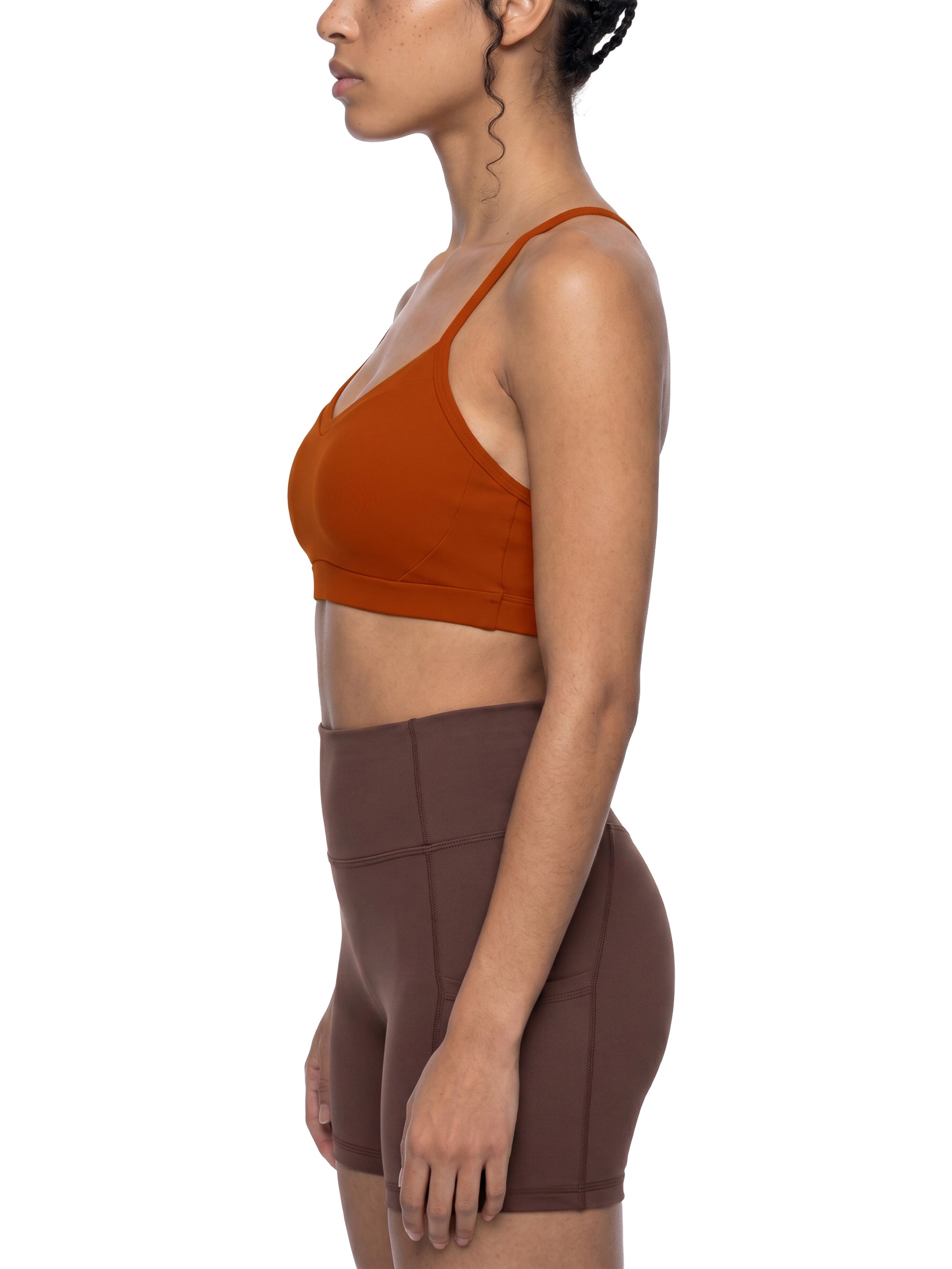 Woman wearing a rust-colored sports bra and brown shorts on a white background